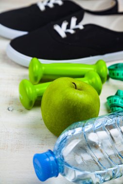 Spor ayakkabıları, halterler, bir şişe su, bir elma ve bir ölçün