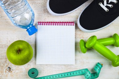 Spor ayakkabıları, halterler, bir şişe su, bir elma ve bir ölçün