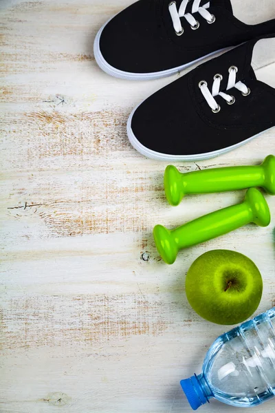 Gym shoes, dumbbells, a bottle of water, an apple and a measurin