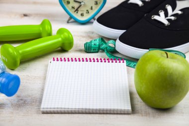 Spor ayakkabıları, halterler, bir şişe su, bir elma ve bir ölçün