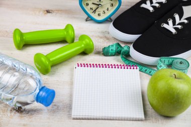 Spor ayakkabıları, halterler, bir şişe su, bir elma ve bir ölçün