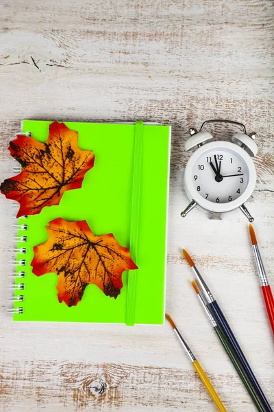 Relógio despertador, cadernos, pincéis e folhas de outono — Fotografia de Stock