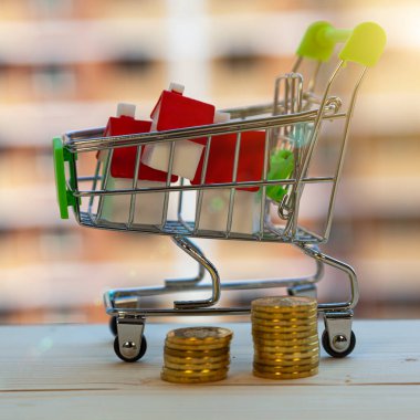 Alışveriş arabasında bir ev ve inşaat halindeki bir binanın arka planında para. Bir mülk satın almak.