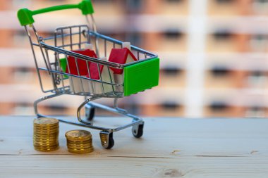 Alışveriş arabasında bir ev ve inşaat halindeki bir binanın arka planında para. Bir mülk satın almak.