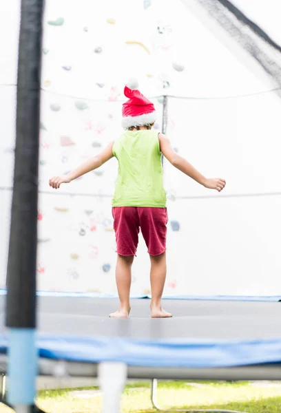 Trambolin Üzerinde Atlama Noel Baba Şapkası Olan Küçük Çocuk — Stok fotoğraf