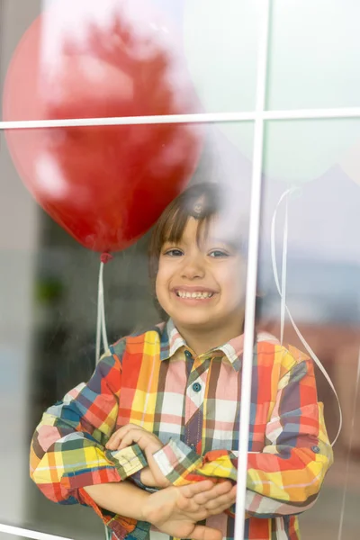 在窗玻璃后面拿着一堆气球的男孩 — 图库照片