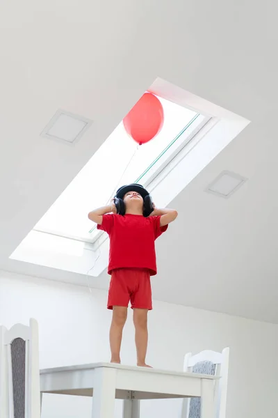 Niño de pie sobre una mesa mientras sostiene un globo —  Fotos de Stock