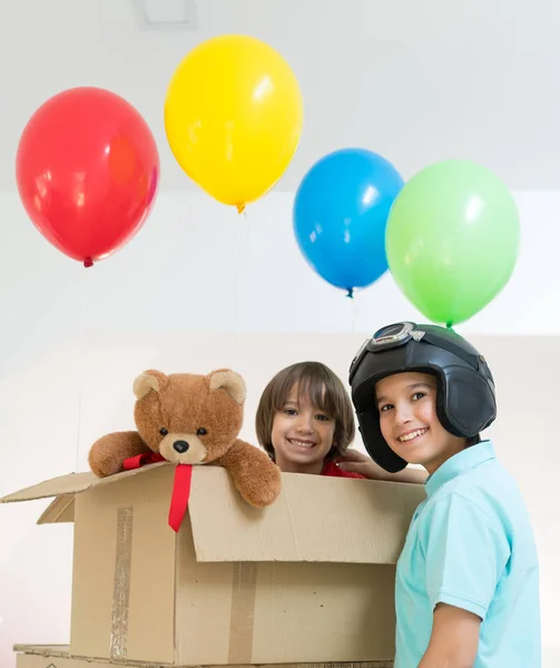 Irmãos felizes brincando com balões e caixa de papelão — Fotografia de Stock