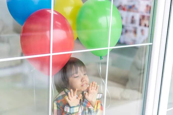 Niño con un montón de globos detrás del cristal de la ventana — Foto de Stock