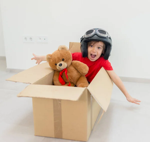 Happy boy flying in a box and wearing a hat with his toy — Stock Photo, Image