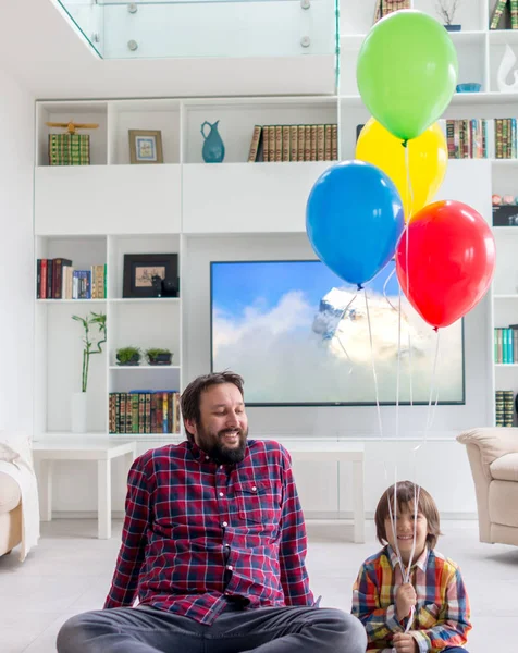 Feliz padre e hijo sentados en el suelo con un montón de globo — Foto de Stock