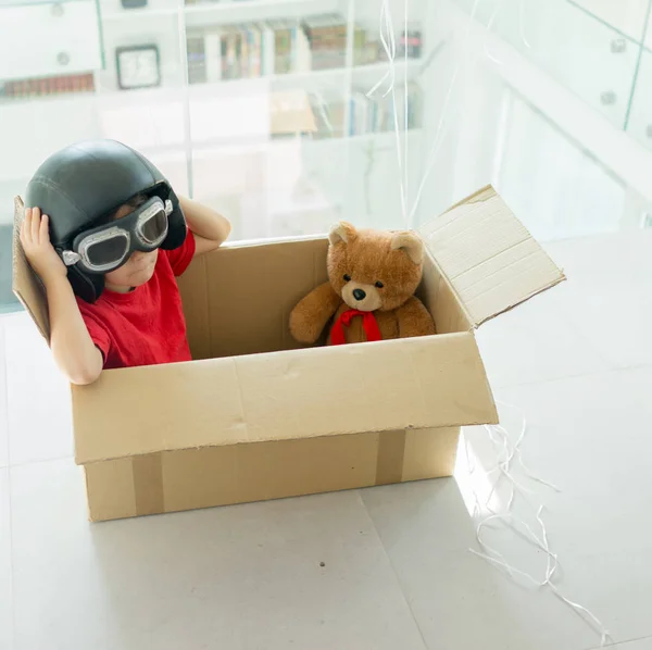 Happy boy flying in a box and wearing a hat with his toy — Stock Photo, Image