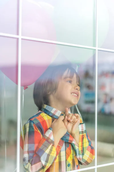 Rapaz com um monte de balões atrás do vidro da janela — Fotografia de Stock