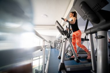 Güzel genç bayan spor salonunda eliptokal makine kullanıyor.
