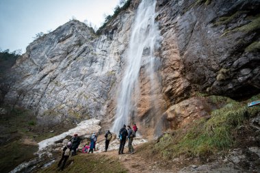 Deneyimli yürüyüşçü takım arkadaşlarıyla şelalenin önünde duruyor.