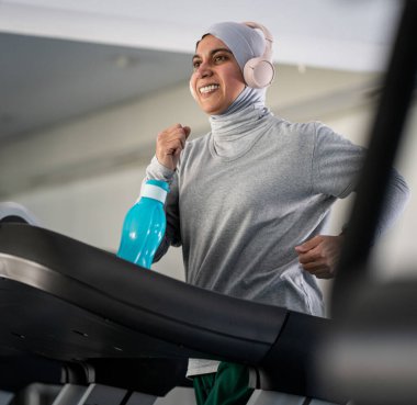 Spor salonunda Koşu bandında Kulaklıklı Müslüman Yetişkin Kadın
