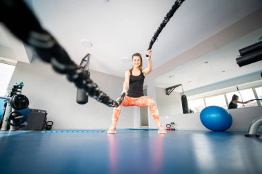 Çekici fit bir kadın spor salonunda halat kullanırken çömeliyor.