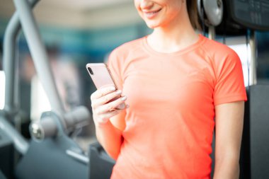 Spor salonunda antreman sırasında telefona bakan sağlıklı genç bir kadın.