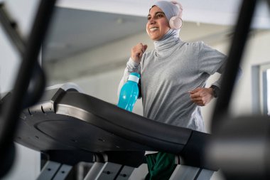Spor salonunda Koşu bandında Kulaklıklı Müslüman Yetişkin Kadın