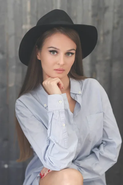 woman in black hat and shirt posing against wooden wall background