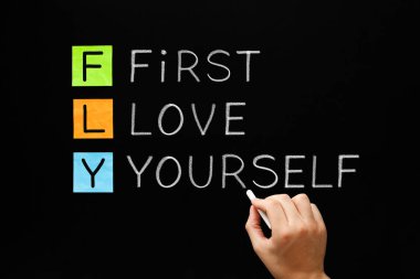 Hand writing FLY - First Love Yourself acronym with white chalk on blackboard. Self-love, acceptance and happiness concept. clipart