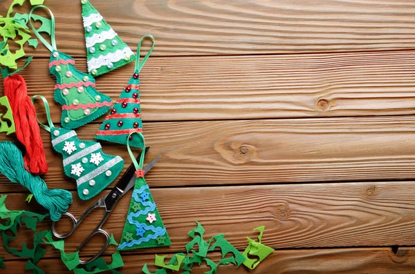 Handmade rustic green felt Christmas tree decorations and scissors flat lying on wooden table