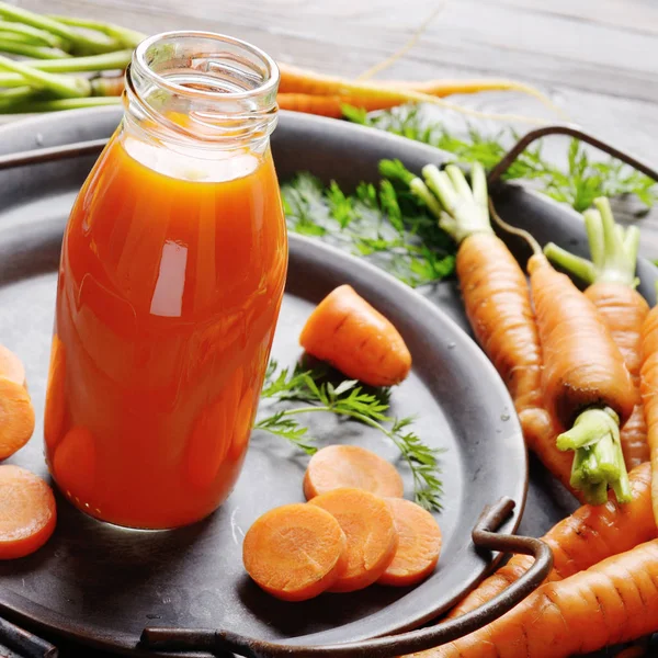 Vegetarian background of old tray with carrots and small bottle