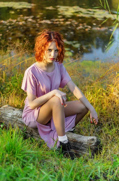 身穿粉色衣服的女人坐在池塘边的圆木上 浅色的Dof — 图库照片