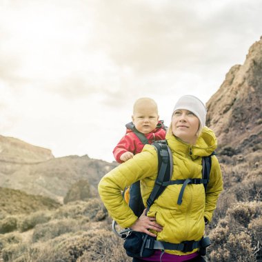 Süper kahraman anne küçük çocuk sırt çantası içinde seyahat ile. Macera çocuk ile Aile gezisi dağlarda hiking. Sırtında, hafta sonu seyahat Tenerife, İspanya tatil yolculuk bebek ile yapılan.