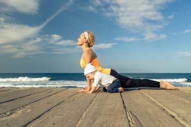 Annesiyle kumsalda, yaz günü oynuyor. erkek bebek. Adamlayken yürümeye başlayan çocuk evlat yoga ahşap beach kaldırımda öğrenme ile.