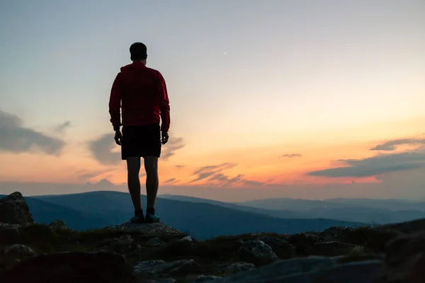 Man celebrating sunset on mountain top. Looking at inspiring view. Trail runner, hiker or climber reached mountain peak, enjoy inspirational landscape on rocky trail Karkonosze, Poland