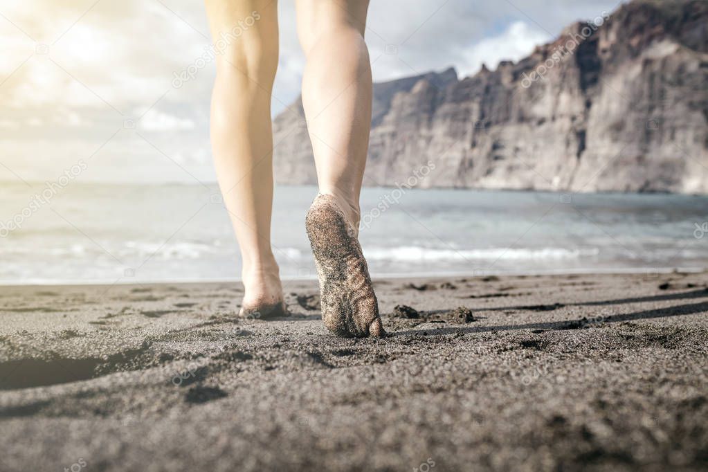 Woman barefoot walking on a beach, summer inspiration. Female naked legs running, walking or jogging on sand at seaside and ocean, inspirational landscape, Tenerife Canary Islands, Spain.