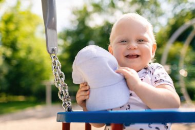Bebek Çocuk Bahçesi alanında oynuyor. Having oyunculuk ile gülen yüz, kameraya bakarak gülümseyen yürümeye başlayan çocuk portresi. Güneşli yaz gün açık havada üzerinde sallanan.