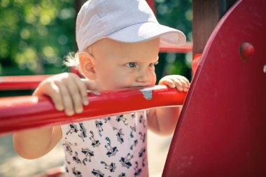 Bebek Çocuk Bahçesi tek başına oynuyor. Uzakta ile mutsuz yüz bakarak yürümeye başlayan çocuk portresi. Bir oyuncak Bahçesi alan açık havada tutan.