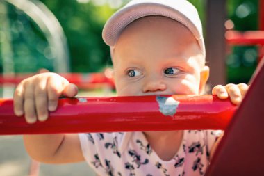 Bebek Çocuk Bahçesi tek başına oynuyor. Uzakta ile mutsuz yüz bakarak yürümeye başlayan çocuk portresi. Bir oyuncak Bahçesi alan açık havada tutan.