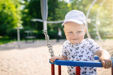 Bebek Çocuk Bahçesi alanında oynuyor. Eğleniyor uzakta mutlu yüz ile seyir gülümseyen yürümeye başlayan çocuk portresi. Güneşli yaz gün açık havada üzerinde sallanan.