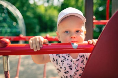 Bebek Çocuk Bahçesi tek başına oynuyor. Mutsuz yüz ile kameraya bakarak yürümeye başlayan çocuk portresi. Bir oyuncak Bahçesi alan açık havada tutan.