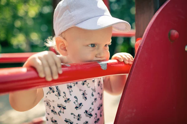 Bebek Çocuk Bahçesi tek başına oynuyor. Uzakta ile mutsuz yüz bakarak yürümeye başlayan çocuk portresi. Bir oyuncak Bahçesi alan açık havada tutan.
