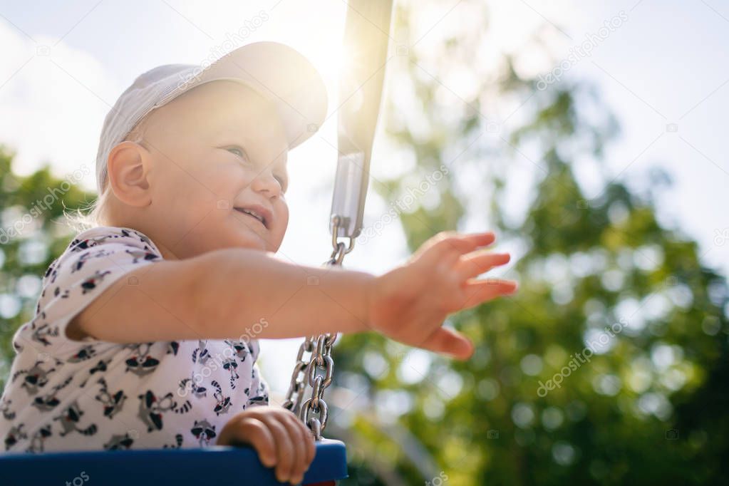 Baby boy playing in playground area. Portrait of smiling toddler looking away with happy face, having fun. Swaying on sunny summer day outdoors.