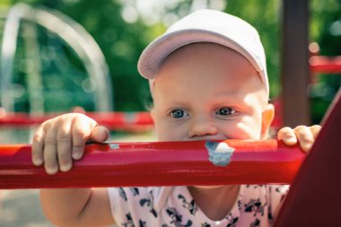 Bebek Çocuk Bahçesi tek başına oynuyor. Uzakta ile mutsuz yüz bakarak yürümeye başlayan çocuk portresi. Bir oyuncak Bahçesi alan açık havada tutan.