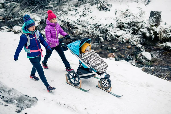 冬の森で母性を楽しむベビーカーで 人の女性 山の風景します パートナーと白い雪に覆われた森の中で子供とハイキングの母 心に強く訴える美しい冬山 ストック写真