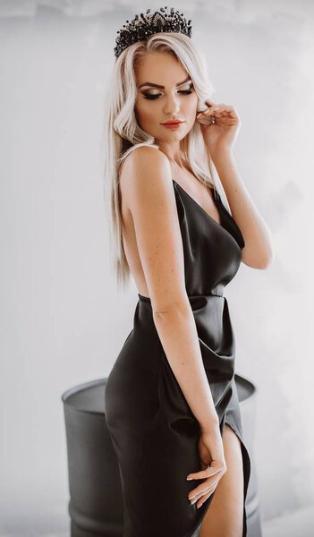 Beautiful young blond woman posing in black sexy dress in studio
