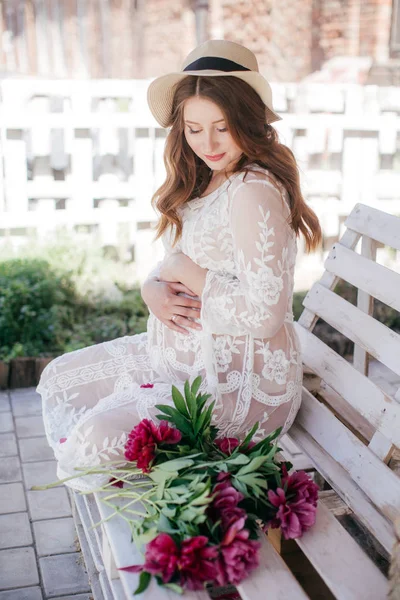 美丽的孕妇在白色礼服和草帽与花 — 图库照片
