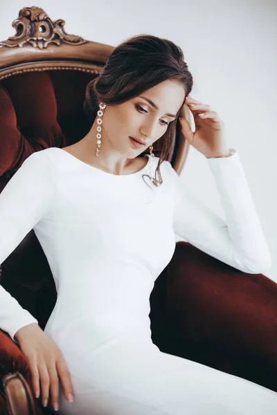 Beautiful young bride in white wedding dress posing on chair