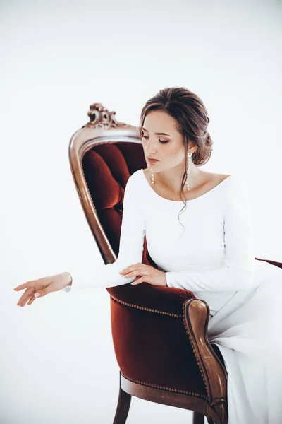 Beautiful young bride in white wedding dress posing on chair