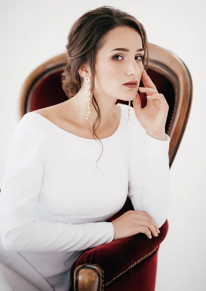 Beautiful young bride in white wedding dress posing on chair