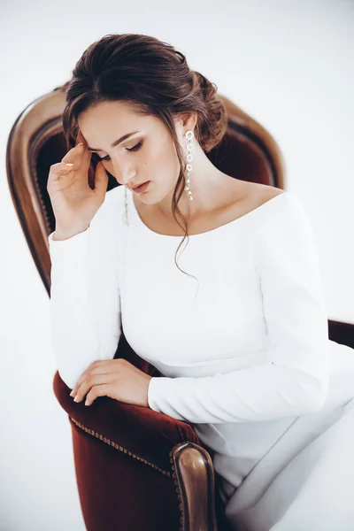 Beautiful young bride in white wedding dress posing on chair