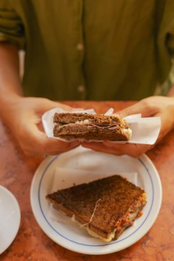 Gen Z orta yaşlı kadın Lizbon 'da geleneksel Portekiz fast food tostu ve pastırma ve peyniri deniyor. Yalnız turizm ve seyahat. Bir serinin parçası.