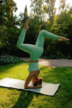 Spor giyim bölümünde genç bir kadın parktaki spor minderinde vücut esnetiyor, yoga yapıyor. Sağlıklı yaşam tarzı, spor. Fitness. Sabah parkında yoga yapan kız. Dizinin bir parçası. Yumuşak odak.