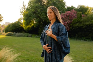 Kadın halka açık bir parkta yoga ve meditasyon yapıyor, gözleri kapalı rahatlıyor. Dikkatli meditasyon konsepti. Sağlıklı olmak. Odak bulanıklığı ve gürültü etkisi yok. Dizinin bir parçası.